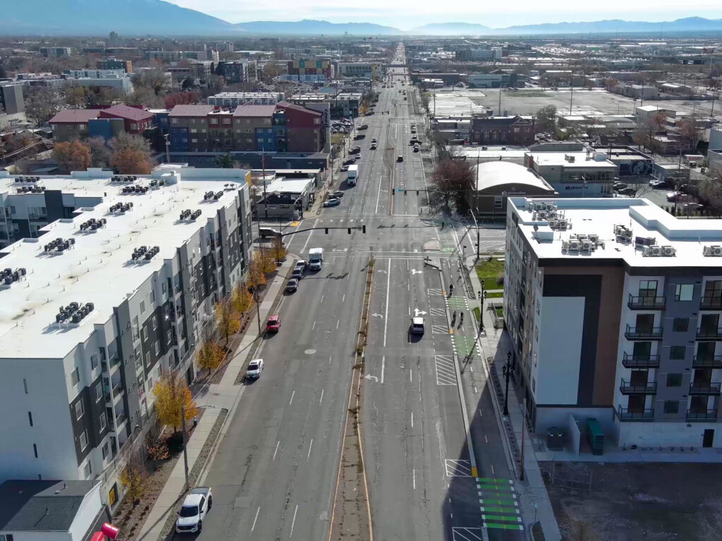 Aerial view of 300 West at 700 South showing a two-way protected bike lane separated from traffic by concrete curb. Green markings highlight bike crossings at intersections and driveways.