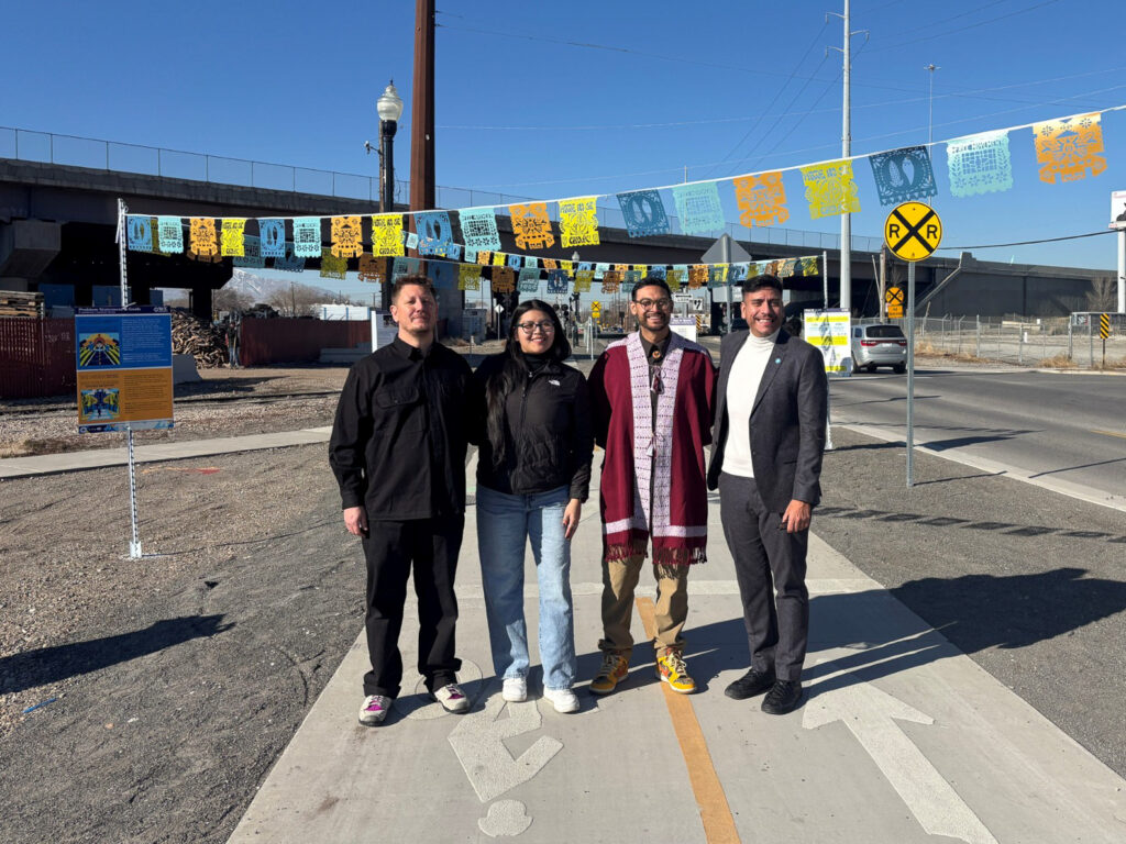 A group of people standing under the papel picado artwork along the 9 Line Trail near the rail crossing.